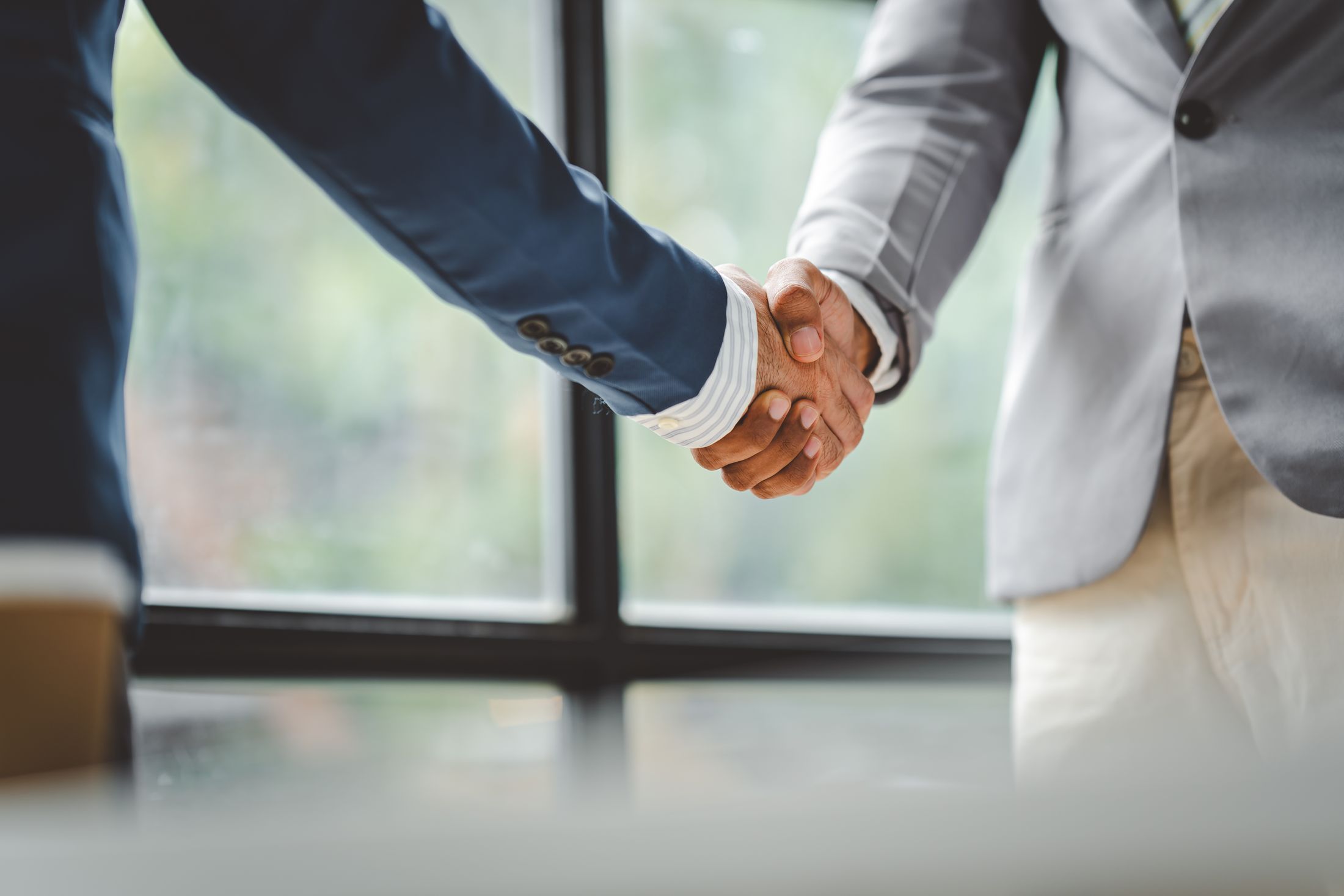 Handschlag zweier Geschäftspartner vor einem Bürofenster